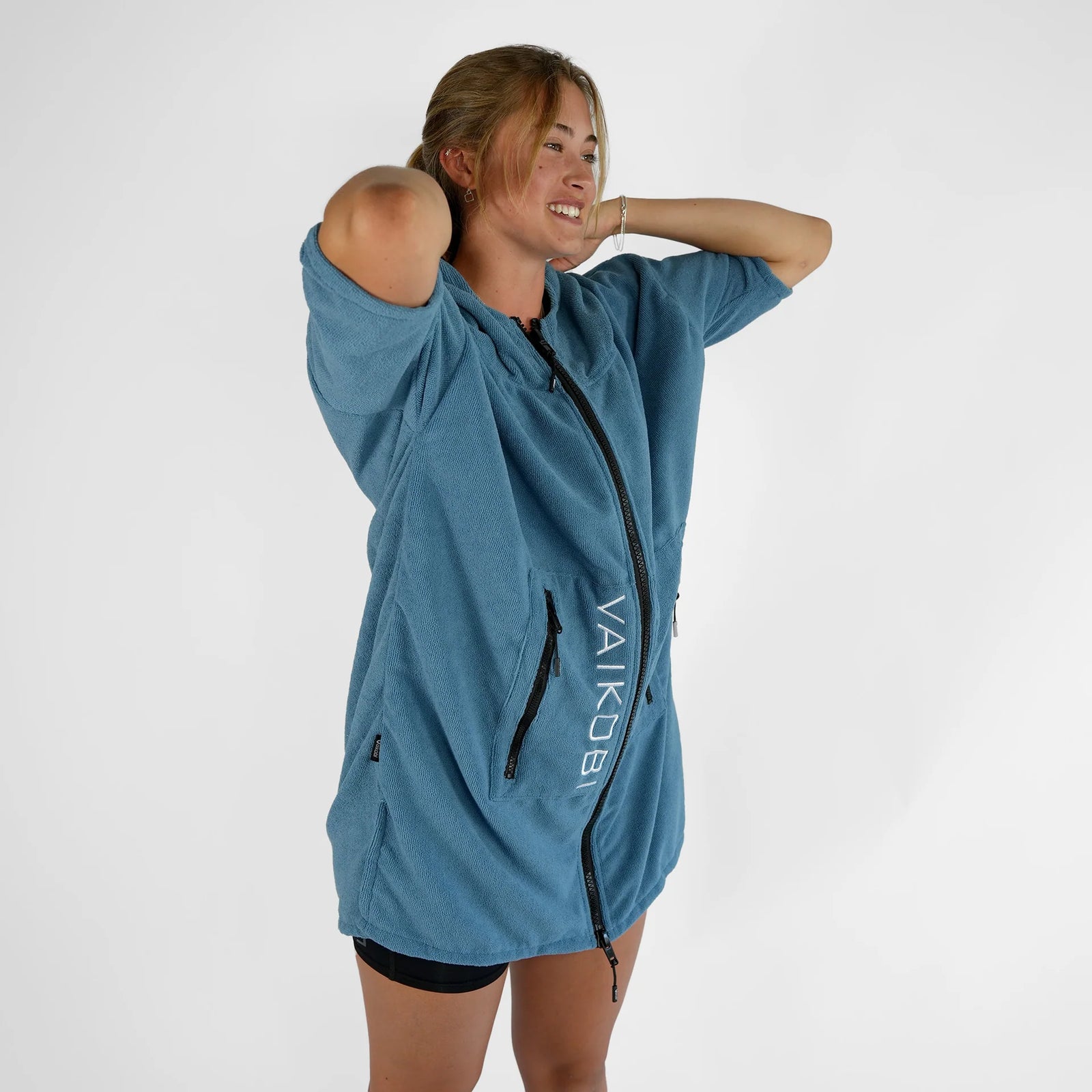 Smiling woman in blue Vaikobi changing robe, demonstrating comfort and practical front zipper.