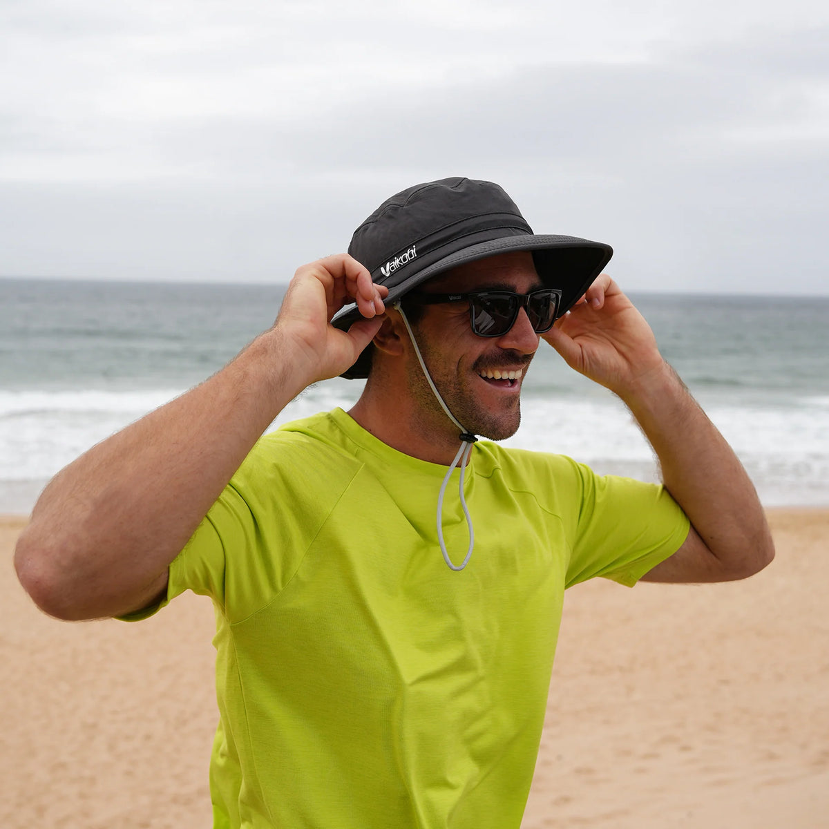 Man adjusting Vaikobi UV Ocean Surf Hat in charcoal at the beach